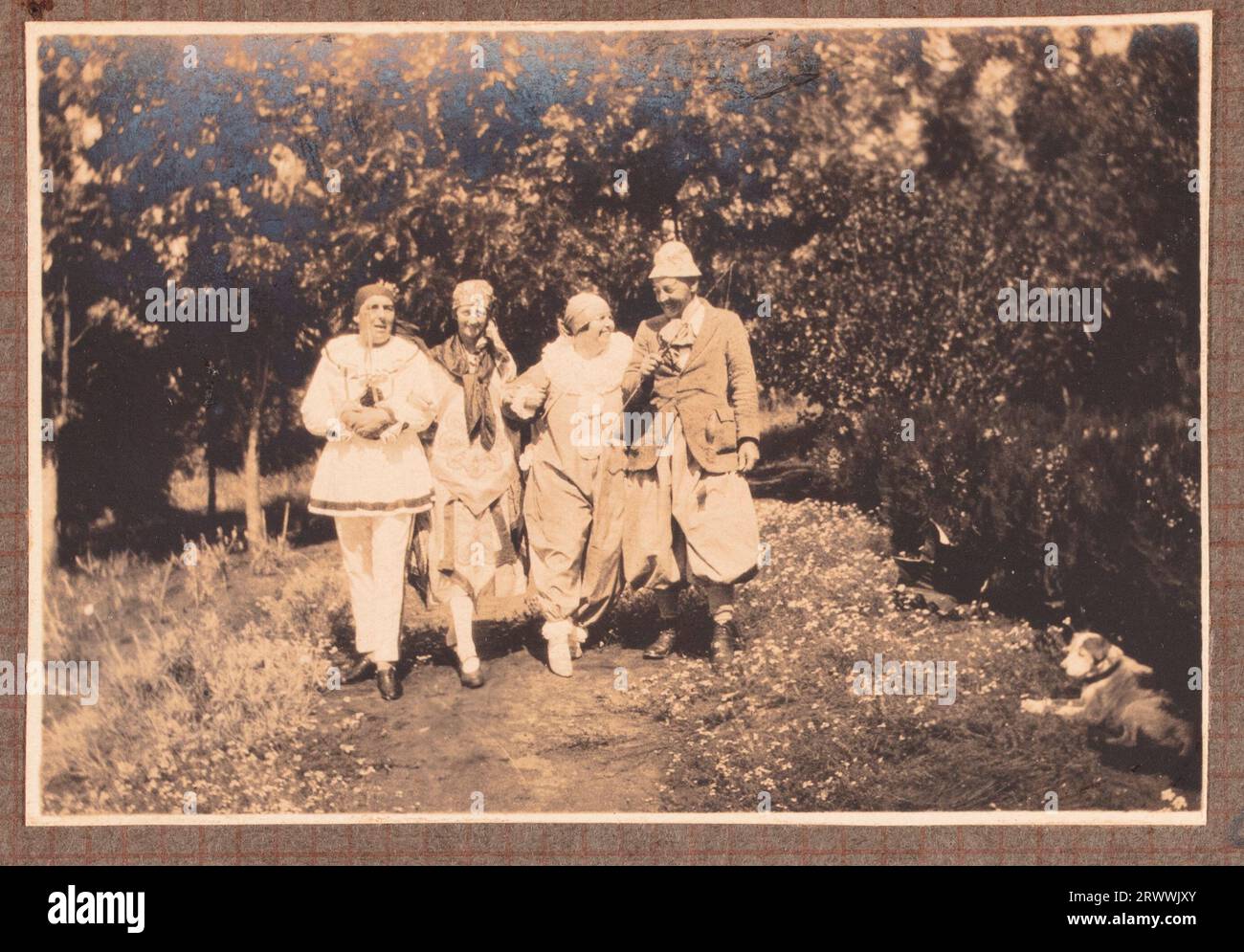 One of a series of photographs showing the Bungeys with friends on a picnic. May Bungey sits with a group of Europeans, including adults and children, in the shade of a tree surrounded by undergrowth. The children are sitting in branches above their heads. Original page caption: Picnic to 'Wamie Hill' Feb: 1927, on Kapiti Plains. Stock Photo
