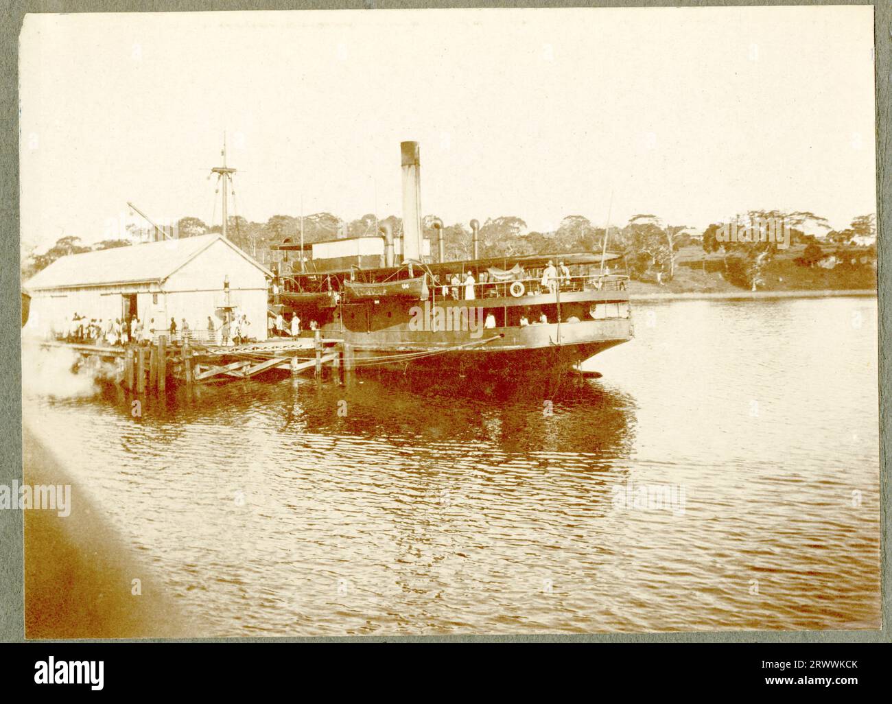 The steamship SS Usoga in the process of loading/ unloading on the pier at Port Bell, Kampala. The ship is partially obscured by a large shed but passengers are visible on upper deck and others, mainly Africans, are waiting to board. Original manuscript caption: SS Usoga. Kampala. Stock Photo