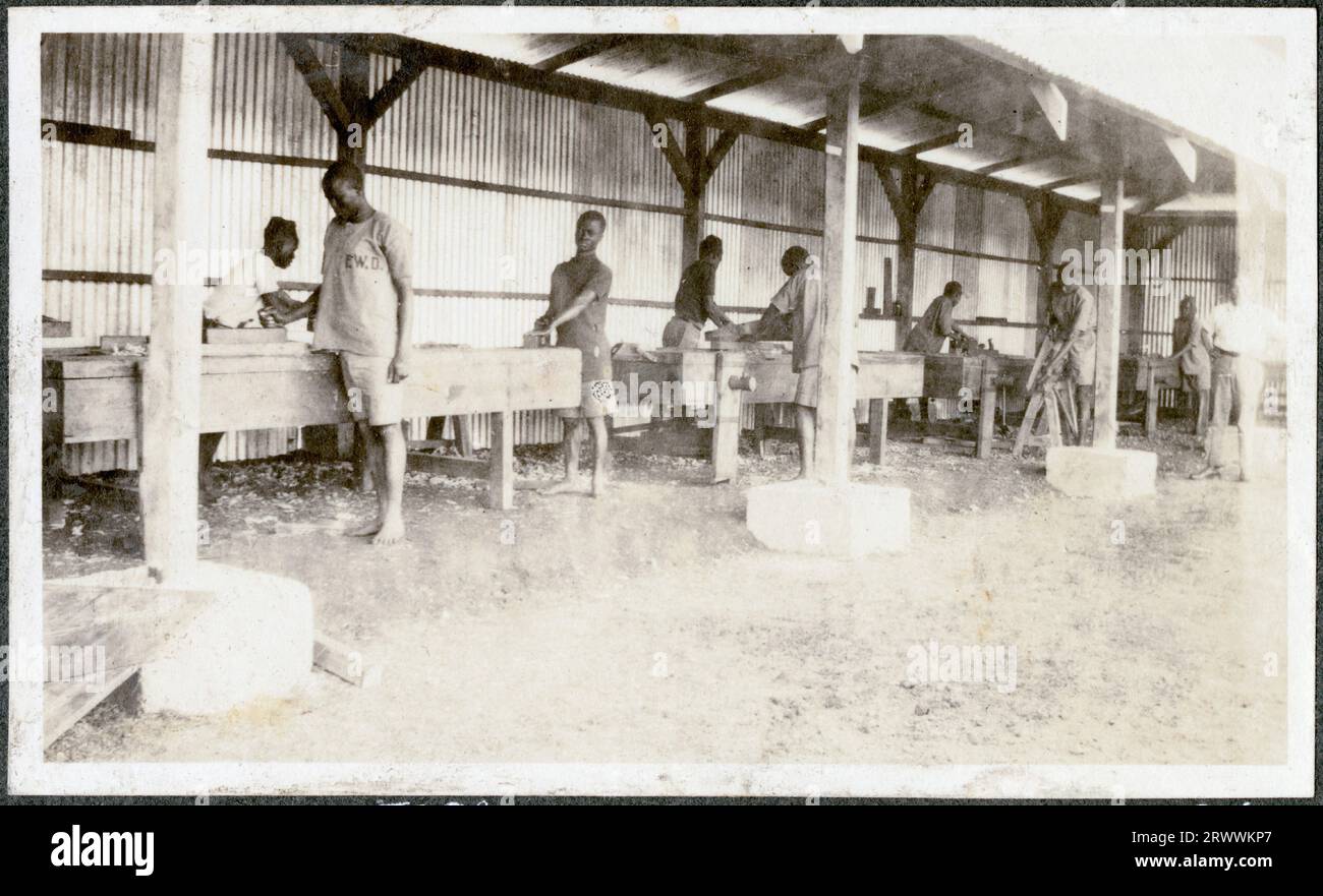 A group of around ten African apprentices of the Nairobi Public Works Department are working on carpentry projects in their outdoor workshops. Charles Bungey, their instructor, is just visible at the right of the image.  Original manuscript caption: Native carpenters P.W.D. Nairobi B.E.A. Later manuscript caption: Charles Bungey's boys. Stock Photo