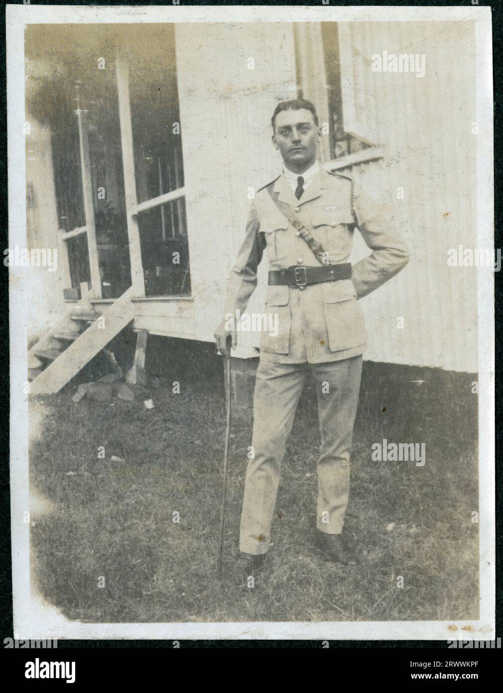 Portrait of Bertie Rand, in military or police officer's uniform and leaning on a cane outside a corrugated iron house with steps up to a veranda.  Later manuscript caption: Bertie RAND, N, J &Y g'father. Stock Photo