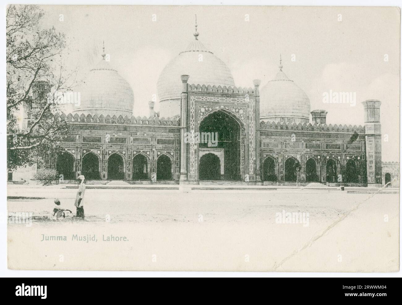 View of large mosque, with three domes, and a front elevation of traditional Islamic design. Identified by printed caption as Jumma Musjid, Lahore. Stock Photo