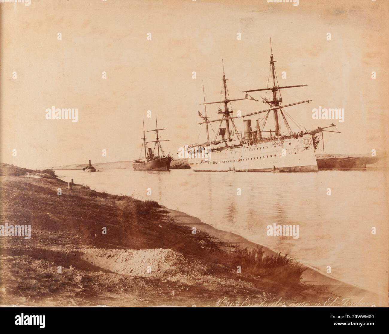View of a single-funnelled troopship with three masts moored on the Suez canal. There is a smaller ship behind with two masts, and a small ship in the distance. Caption inscribed on negative: No. 107 Euphrates [illegible]. Handwritten caption reads: 1893 Her Majestys Troopship Euphrates in Suez Canal. Stock Photo