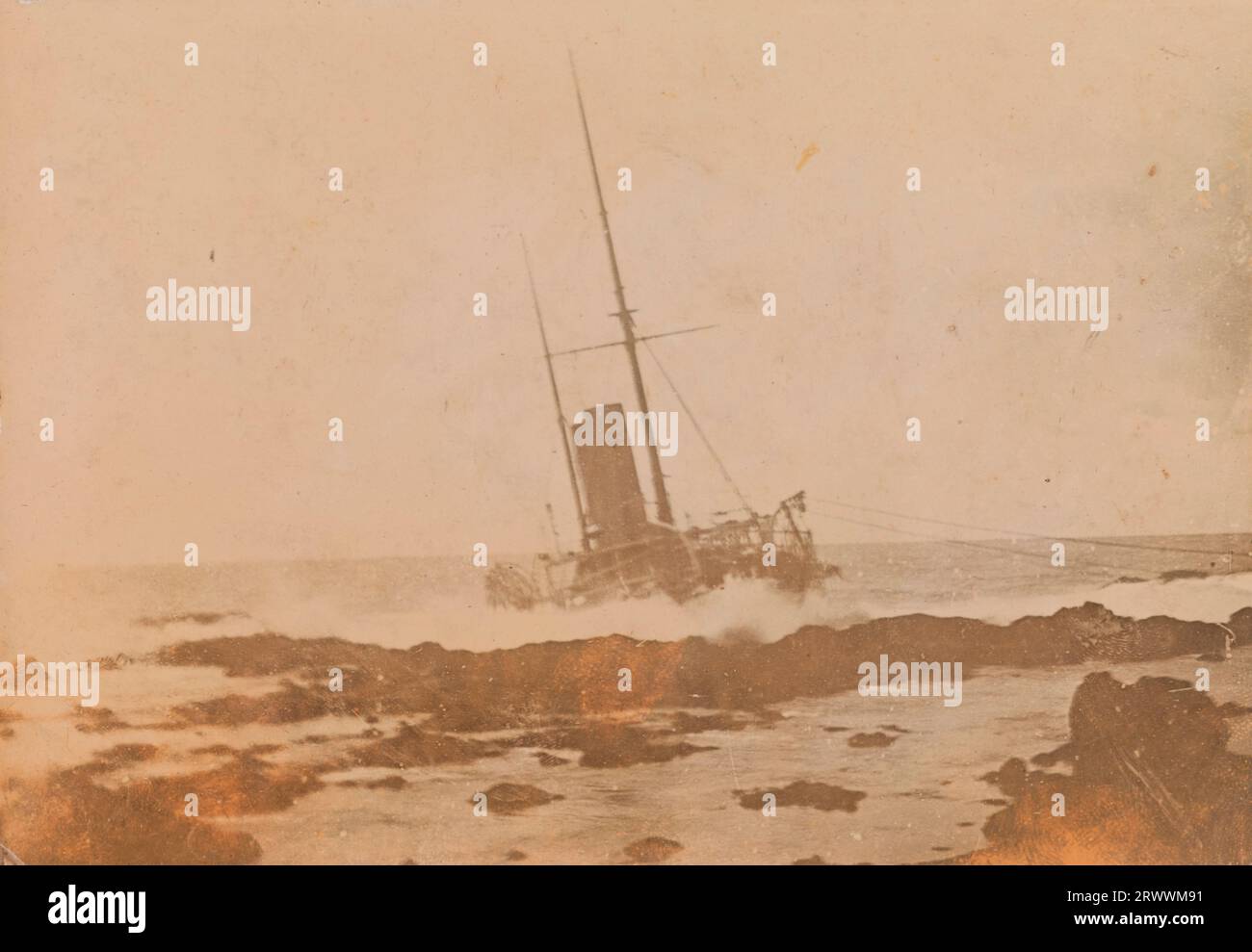 View of a two-funnelled, two-masted ship wrecked on coastal rocks at Mauritius. While the bow is mainly above water the stern section is submerged. Handwritten caption reads: Wreck of R.I.M.S. Warren Hastings. Stock Photo