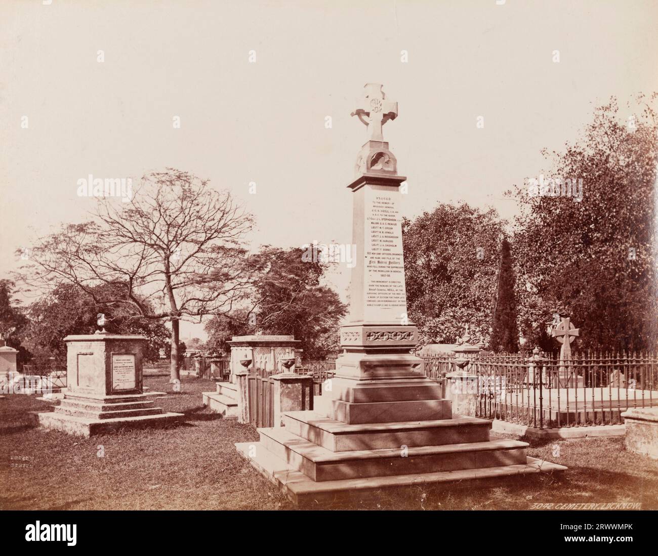 View of a large military memorial mounted with a cross, located in a cemetery. The memorial engraving reads 'To the memory of Brigadier General J C N Neill' and the men of the First Madras Fusiliers, soldiers who fell in the Siege of Lucknow (1857). The memorial is surrounded by other tombs with a manicured lawn and trees. Inscribed on negative: Frith's Series. 3042 Cemetery, Lucknow. Caption reads: Neill's Tomb, Lucknow. Stock Photo