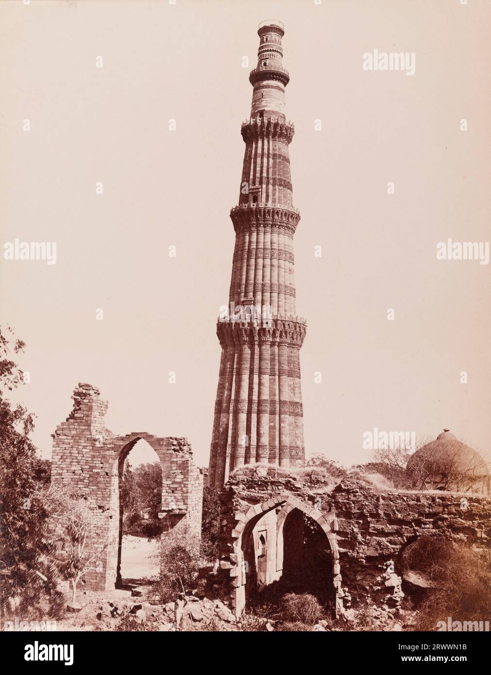 View of the Qutub Minar. At 72.5 metres tall, this was built as a celebratory victory tower to accompany the Quwwat-ul-Islam mosque. It is surrounded by ruined walls and a small domed structure. Inscribed on negative: Frith's Series. 1251 Kutub Minar. Caption reads: The Kutub Minar, Delhi. Stock Photo