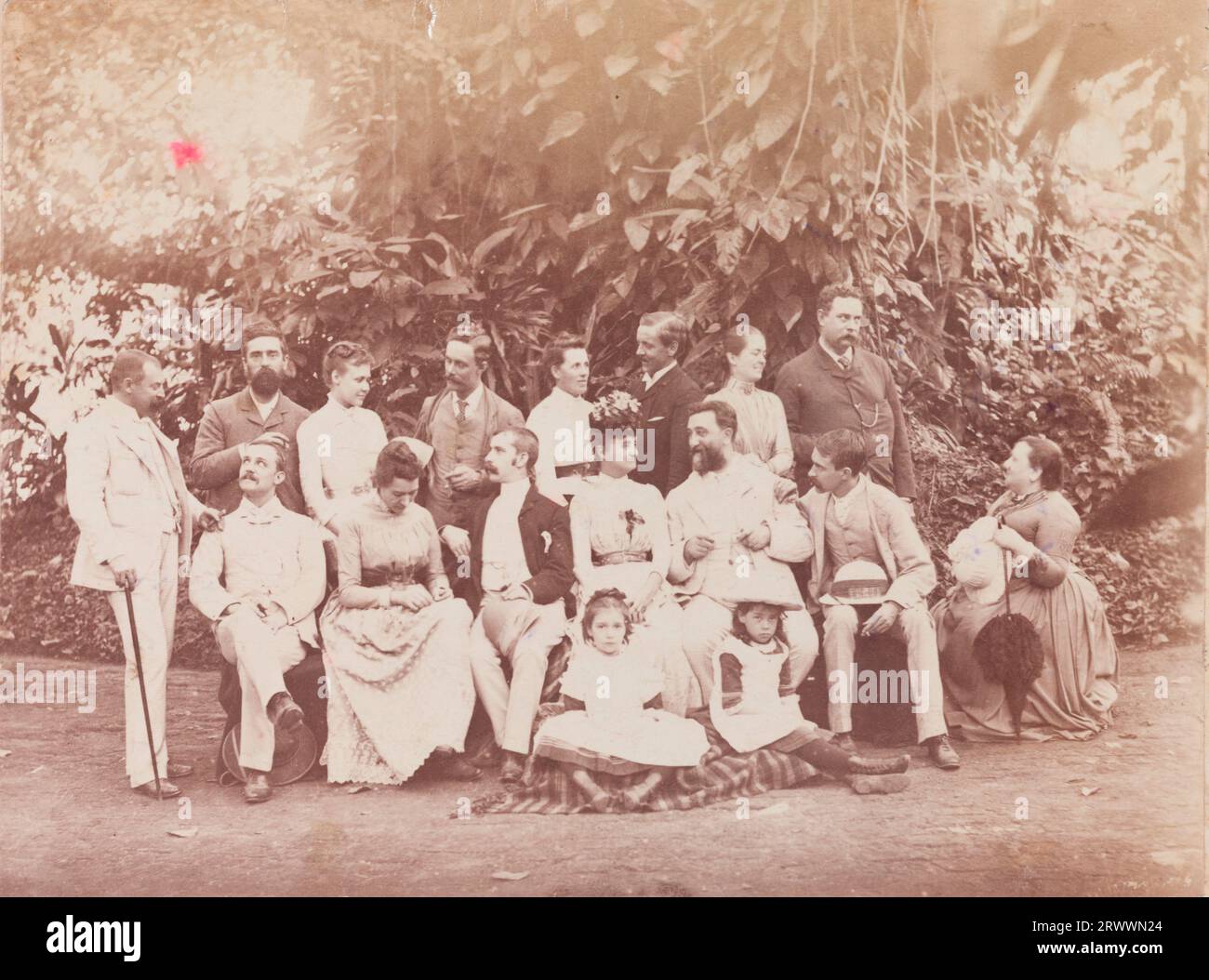 A group portrait of European men and women in formal dress posing outside, in the Botanical Gardens in Calcutta. 8 stand at the back, 7 are seated in front and two young girls sit on a rug at their feet. Caption reads: Xmas 1889. Stock Photo