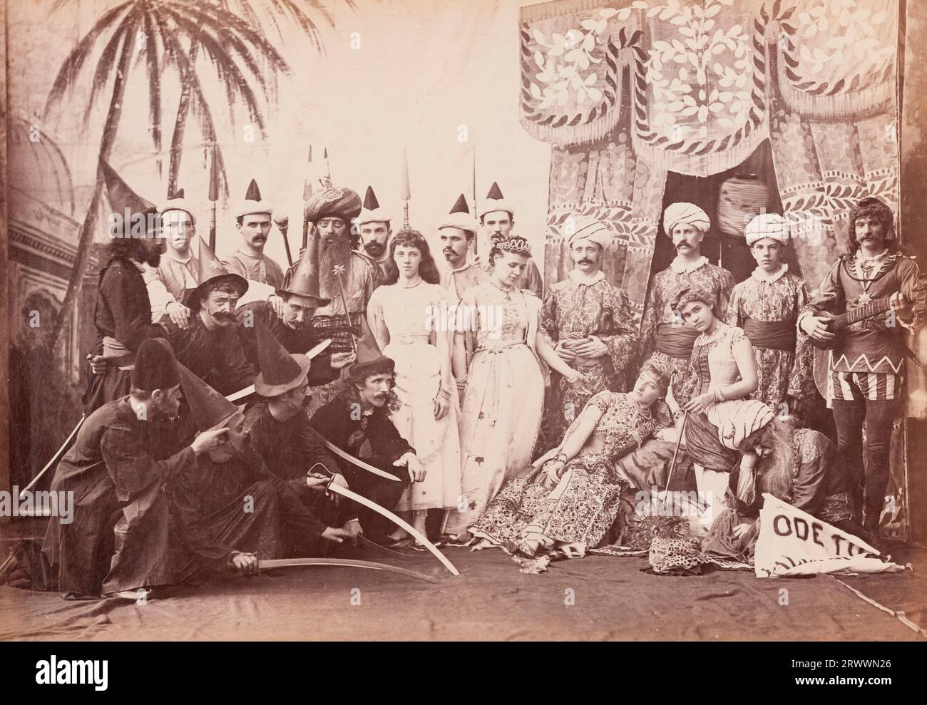 Group portrait of European men and women dressed in costumes for a theatrical production of Lalla Rookh. They pose on a stage with painted backdrops and set behind them, dressed in a variety of orientalist and medieval costumes. Lalla Rookh is a romance by Thomas Moore, published in 1817. Caption reads: Lalla Rookh. Stock Photo