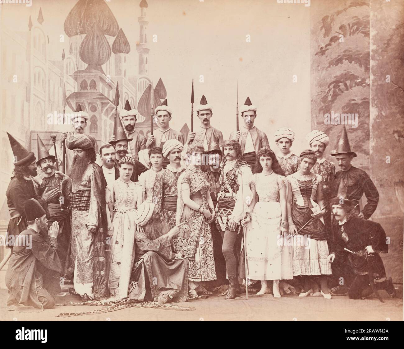 Group portrait of European men and women dressed in costumes for a theatrical production of Lalla Rookh. They pose on a stage with painted backdrops and set behind them, dressed in a variety of orientalist and medieval costumes. Lalla Rookh is a romance by Thomas Moore, published in 1817. Caption reads: Lalla Rookh. Stock Photo