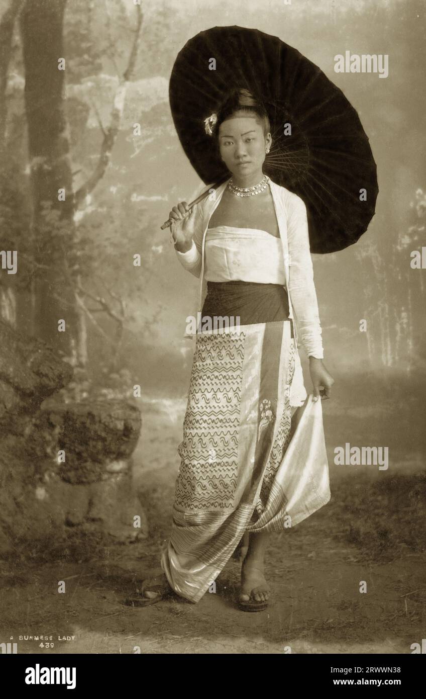 Portrait of a Burmese woman in traditional dress including a silk longyi (wrapped cloth skirt). She holds a parasol and wears a jewelled necklace and earrings. Caption inscribed on negative: A Burmese Lady 439. Handwritten caption reads: A Burmese Lady. Stock Photo