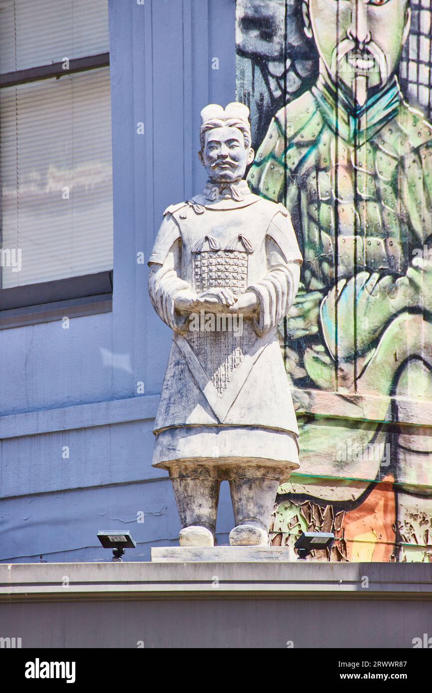 Chinese man statue on corner of building rooftop with wall mural behind