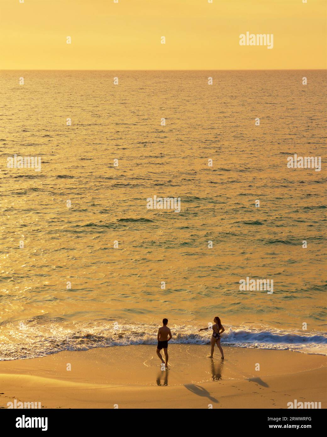 A young man and woman at the water's edge near sunset in bushfire haze conditions at North Beach in Perth, Western Australia Stock Photo