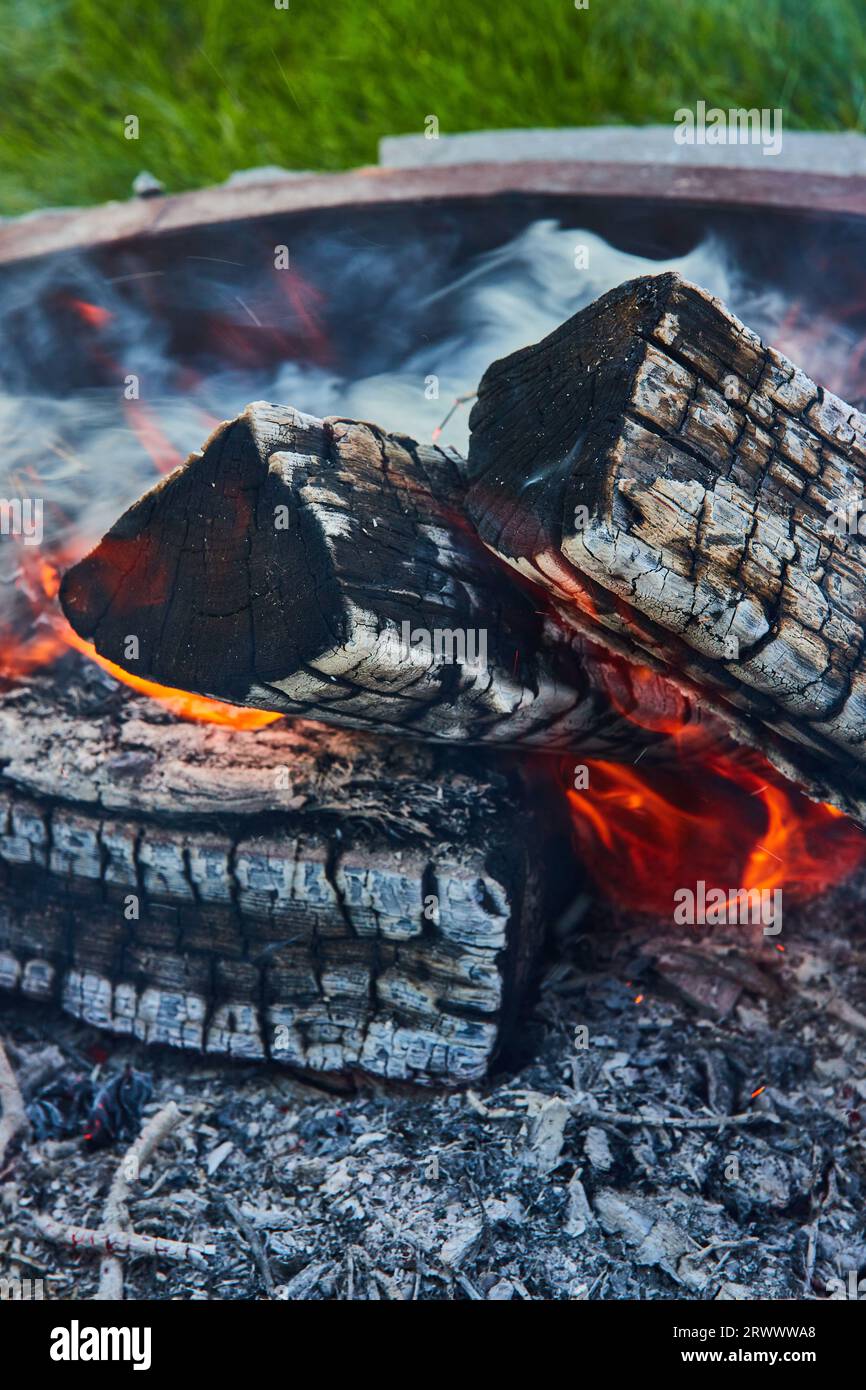 Ashen logs in dying fire inside round fire pit with smoke billowing