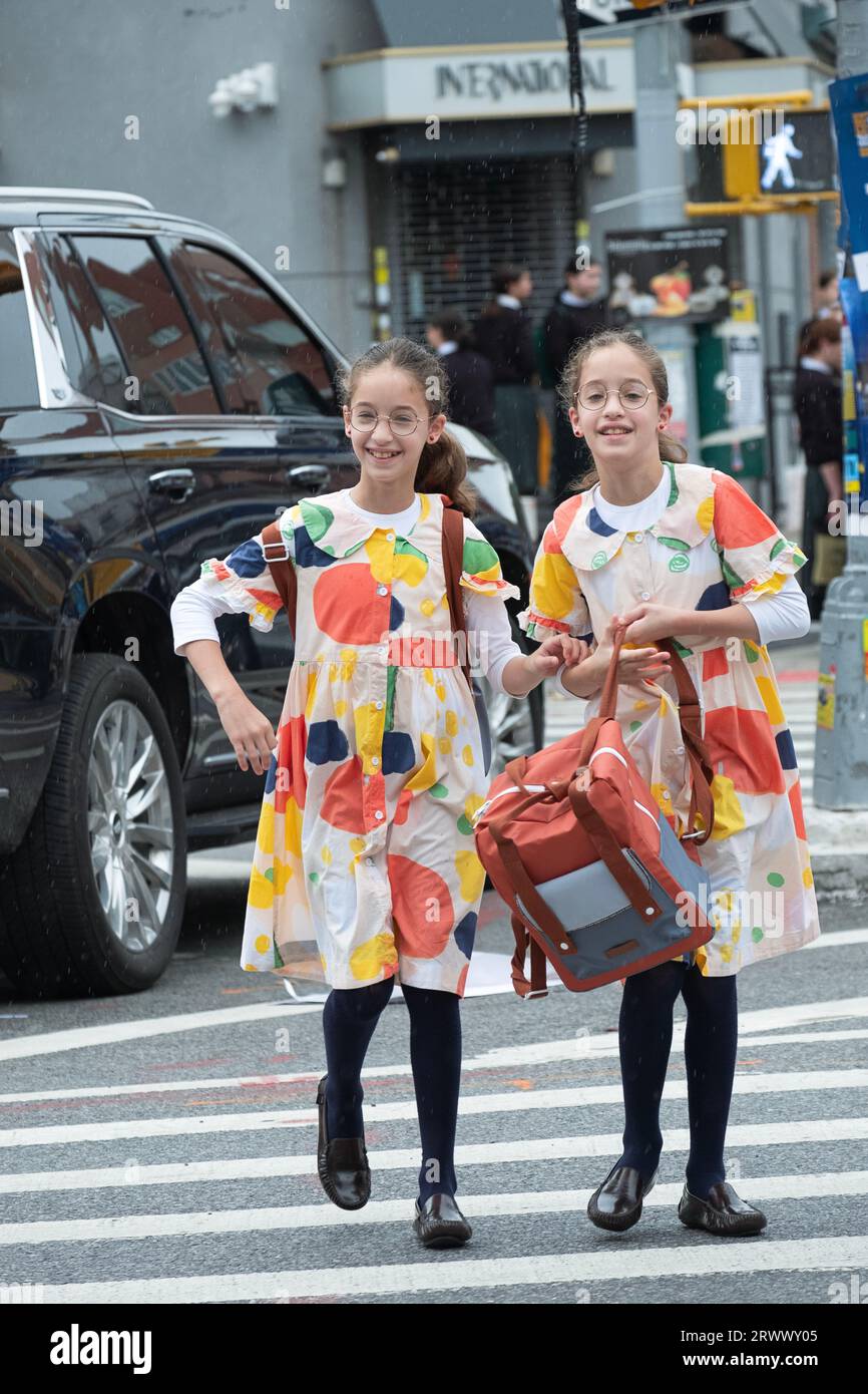 Twin sisters in identical dresses cheerfully head off to school. In Williamsburg, Brooklyn, New York. Stock Photo