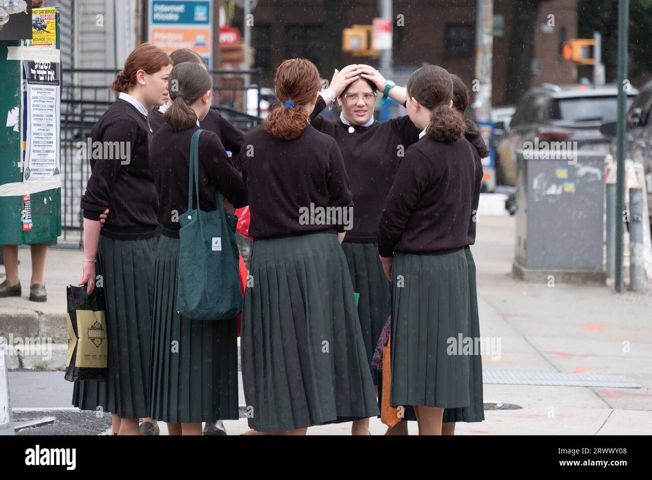 In a light drizzle, orthodox Jewish girls socailze while waiting for a school bus. On Lee Avenue in Williamsburg, Brooklyn, New York. Stock Photo