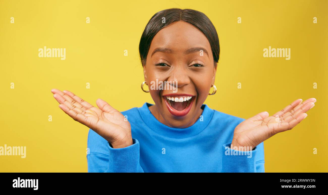 Shocked woman holds palms up in disbelief, yellow studio background Stock Photo