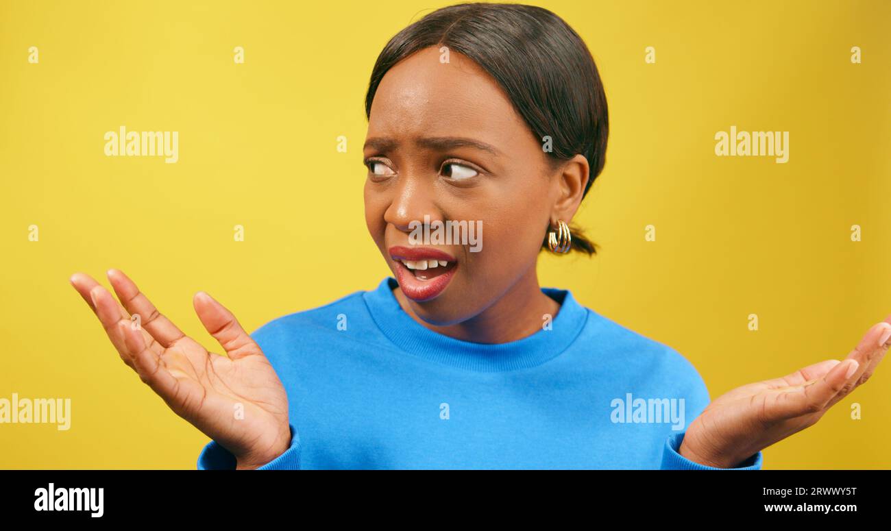 Shocked woman holds palms up in disbelief, yellow studio background Stock Photo