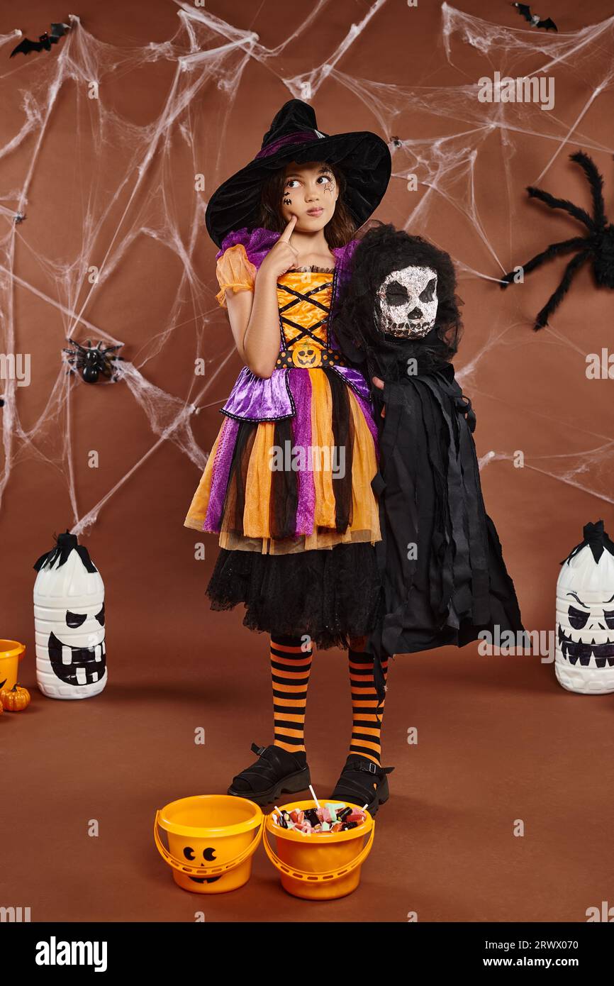preteen girl in witch hat with spooky toy and touching her cheek and