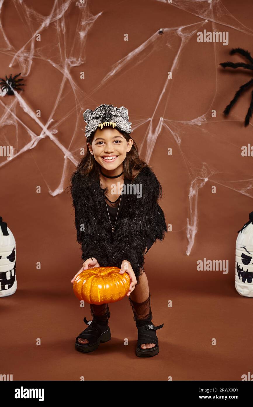 preteen girl bends over with pumpkin in hands with lanterns and spiders