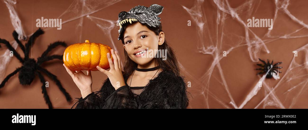 preteen girl holds pumpkin in her hands aside wearing wolf mask