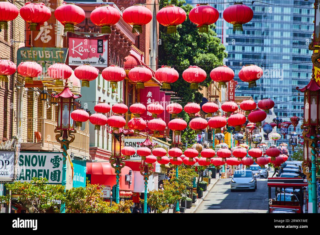Strings of red Chinese lanterns over busy road with white cars and Chinatown shops Stock Photo