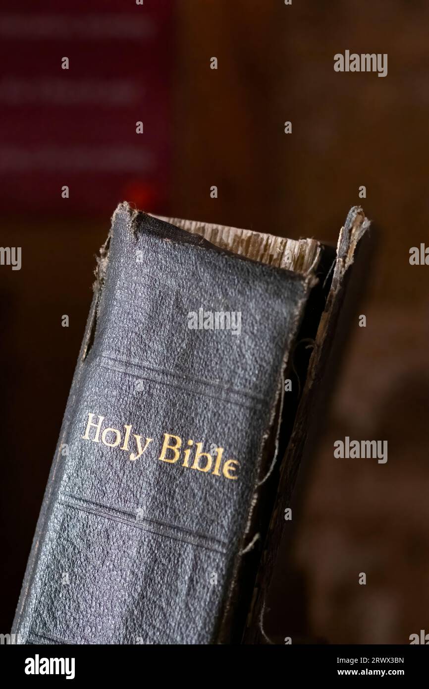 An old book of the Holy Bible. The Bibles binding is broken and its  front cover is hanging off. The words holy Bible are marked on the books spine Stock Photo
