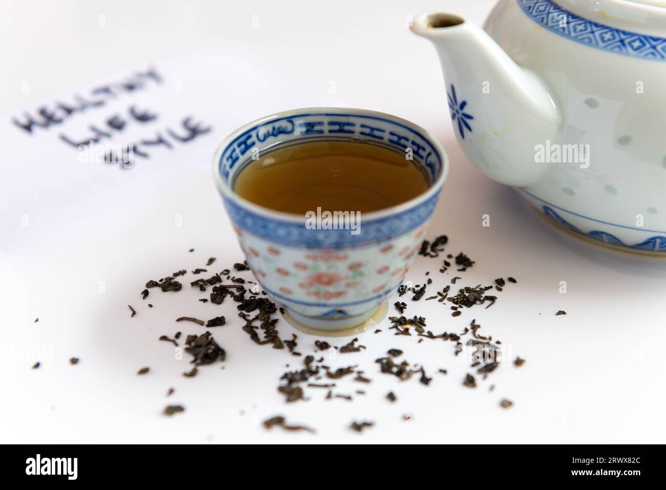 A teapot and a cup of green tea with loose tea leafs isolated in white