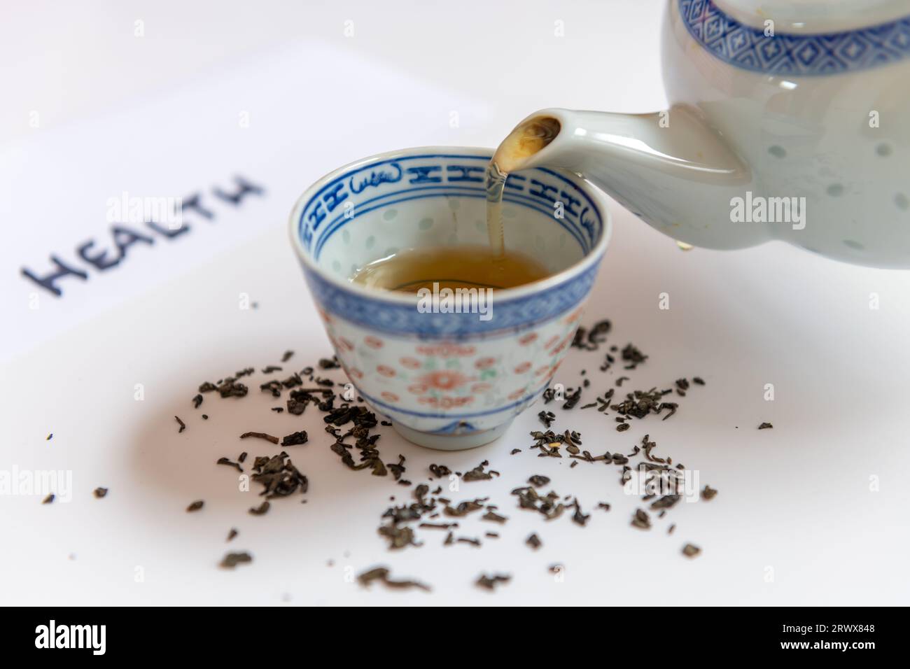 A teapot pouring a cup of green tea with loose tea leafs isolated in