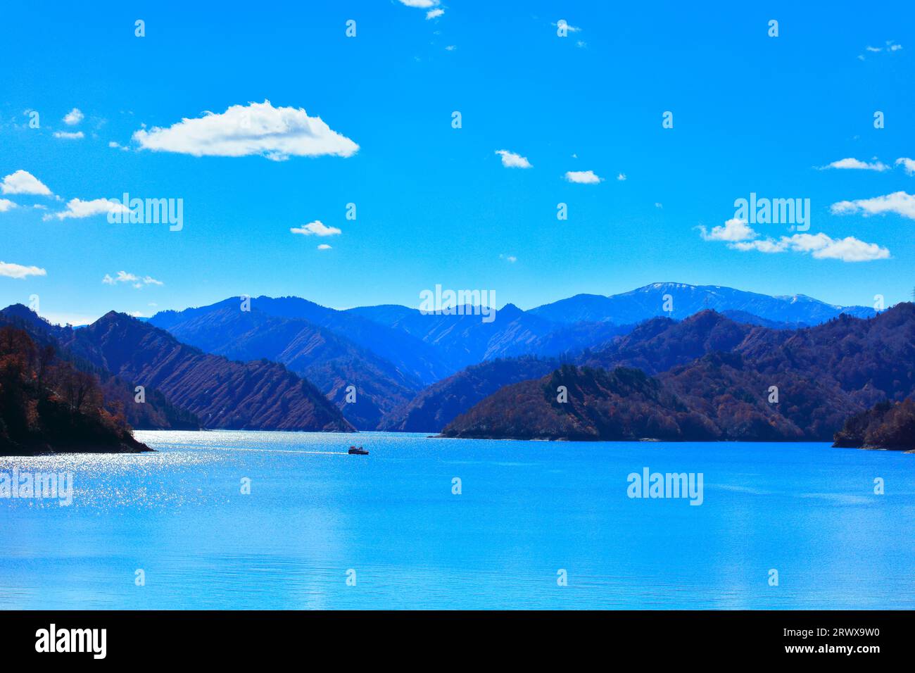 A sightseeing boat and snow-capped mountains at Okutadami Dam in autumn Stock Photo