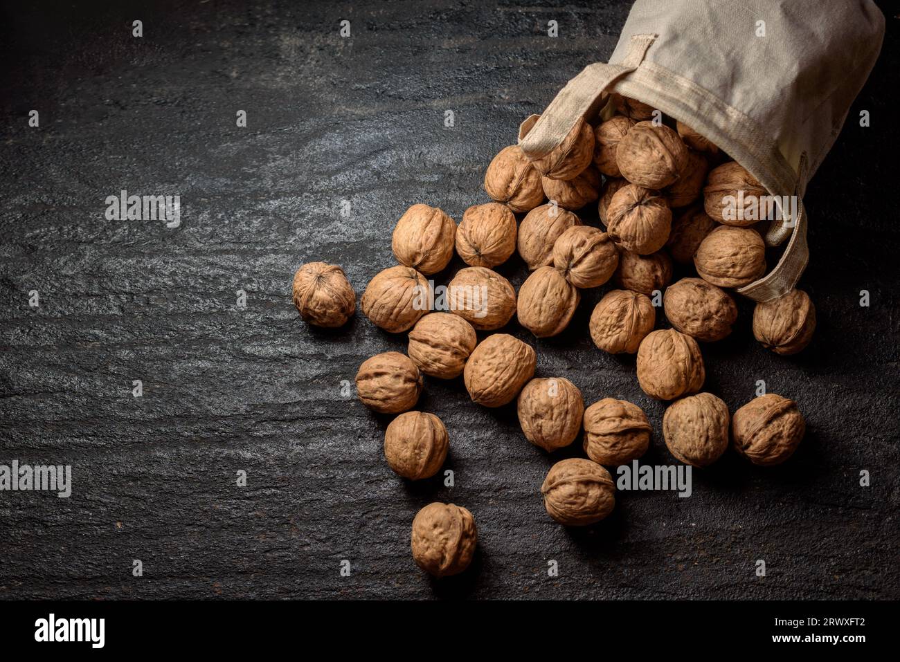 Walnuts in a bag scattered on dark background Stock Photo
