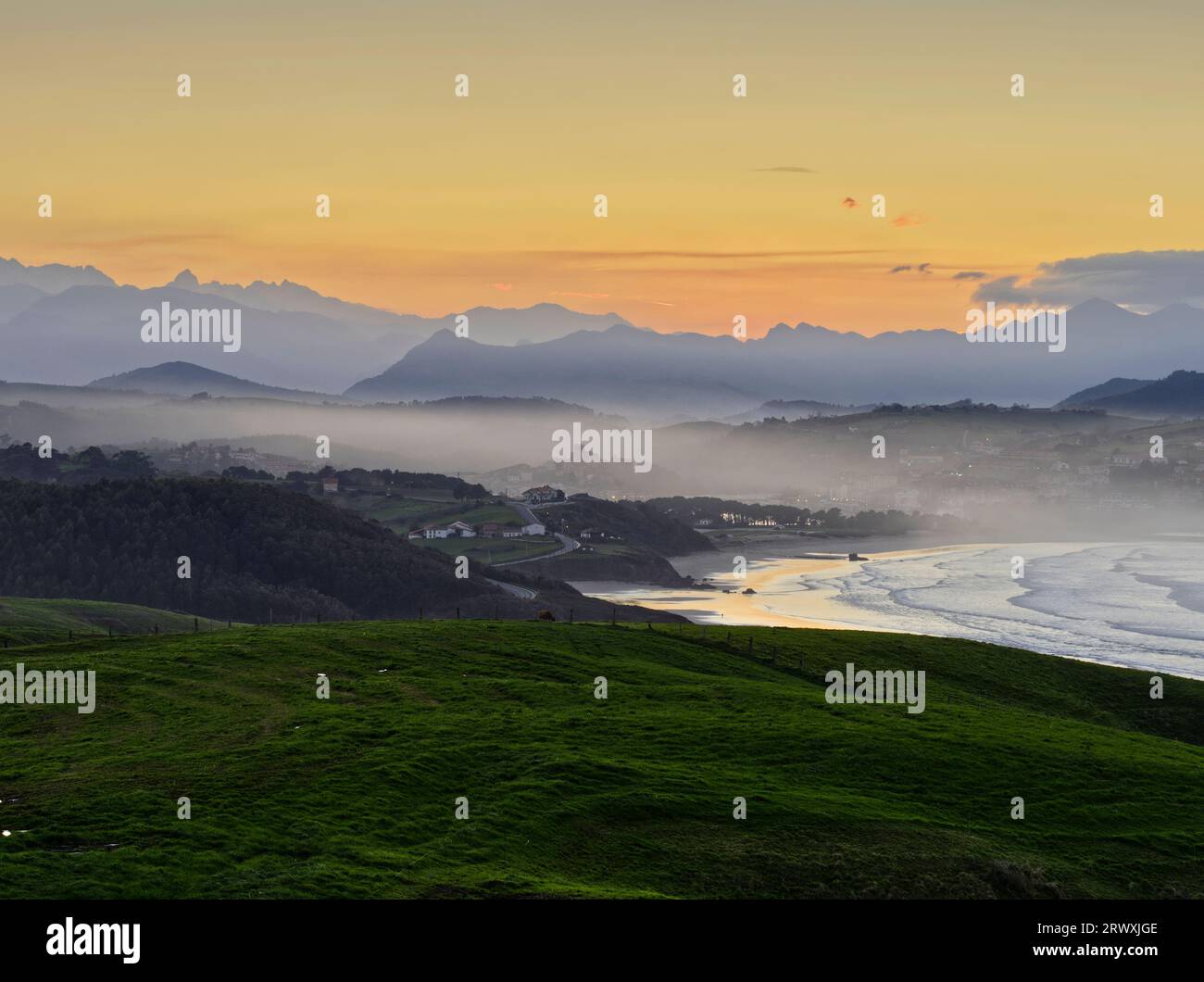 The fishing village of San Vicente de la Barquera, framed at sunset between the Cantabrian Sea, the meadows and the mountains of the Picos de Europa. Stock Photo