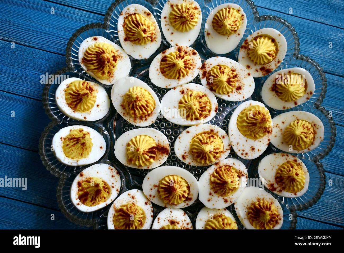Deviled eggs in a decorative glass dish on a bright blue wooden background viewed from above Stock Photo