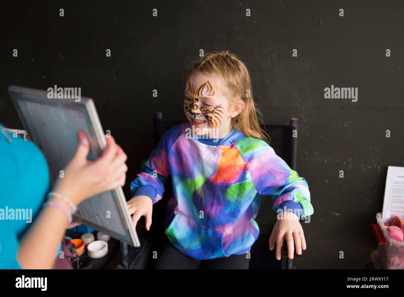 Young girl looking into a mirror and looking happy with her face painting of a leopard. Stock Photo