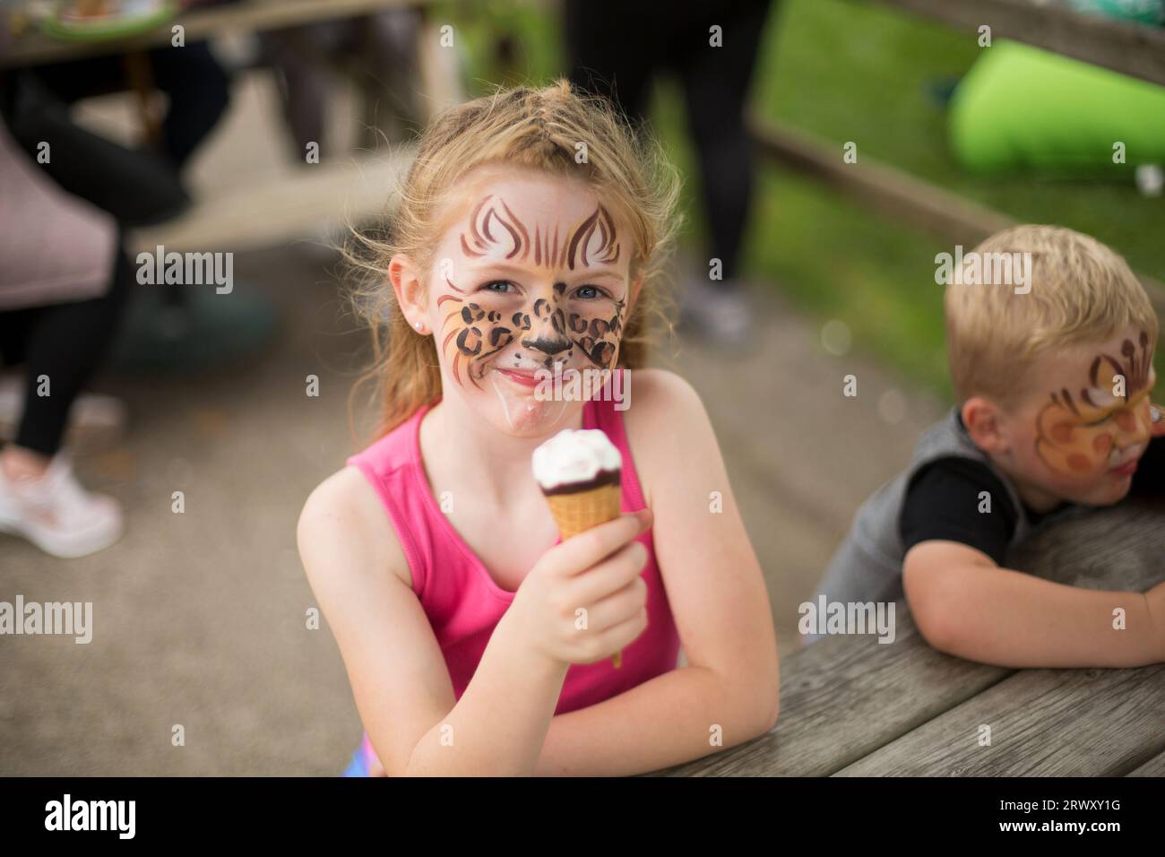 Young girl with a leopard face paint eating ice cream and smiling. Stock Photo