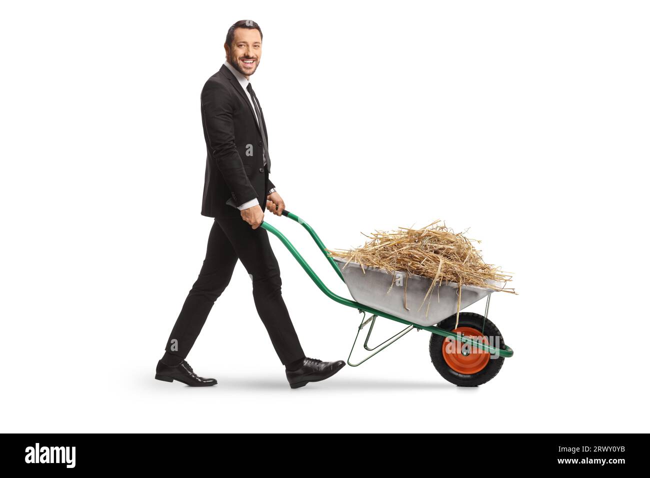 Full length profile shot of a businessman walking with hay in a wheelbarrow isolated on white background Stock Photo