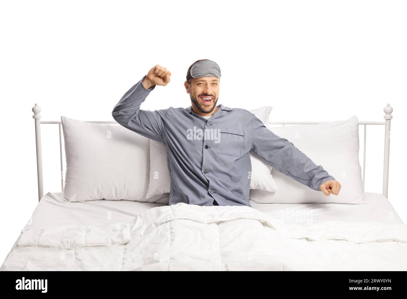 Happy young man with a sleeping mask stretching in a comfortable bed isolated on white background Stock Photo