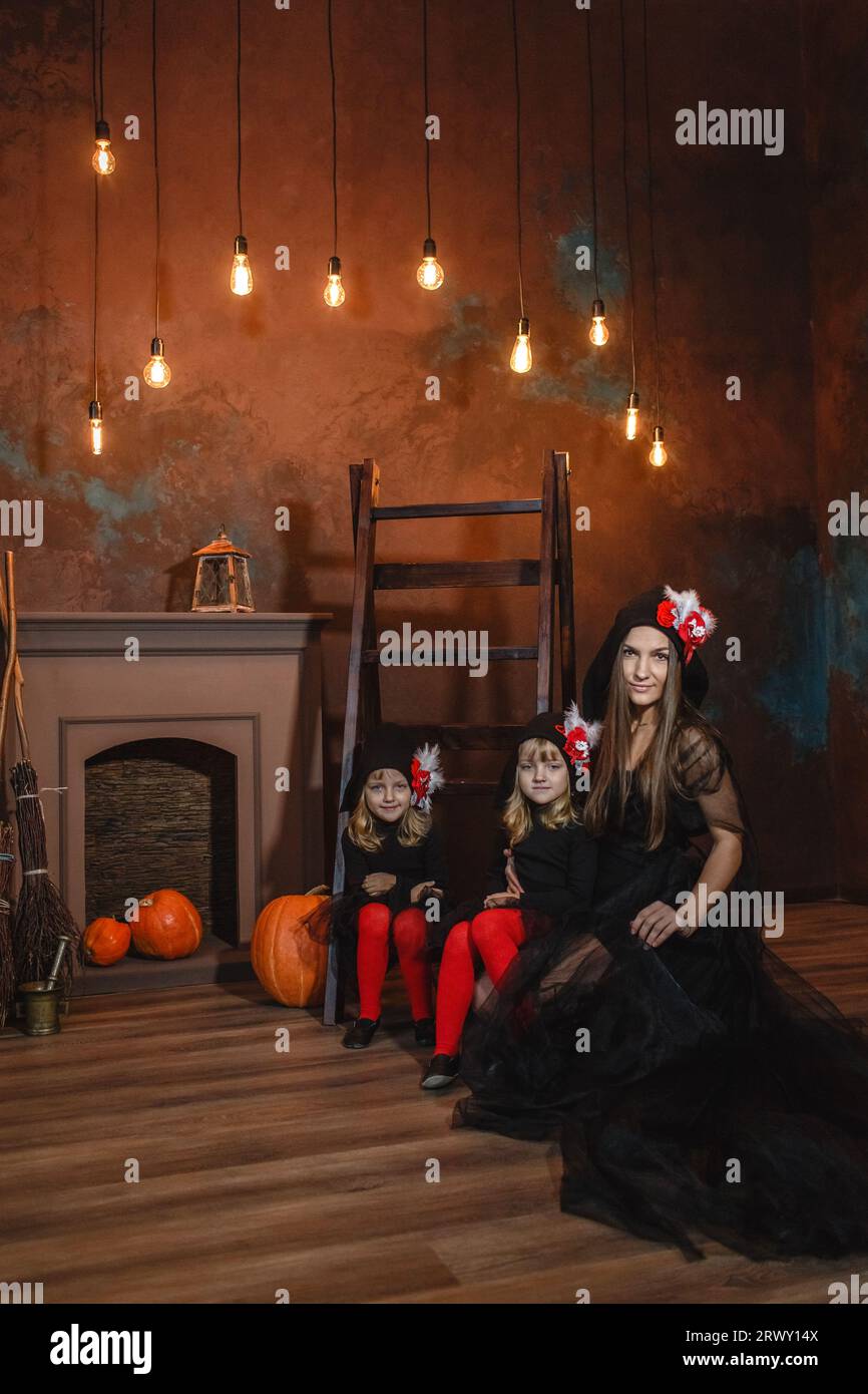 Girls with their mother in witch costumes near the fireplace on the