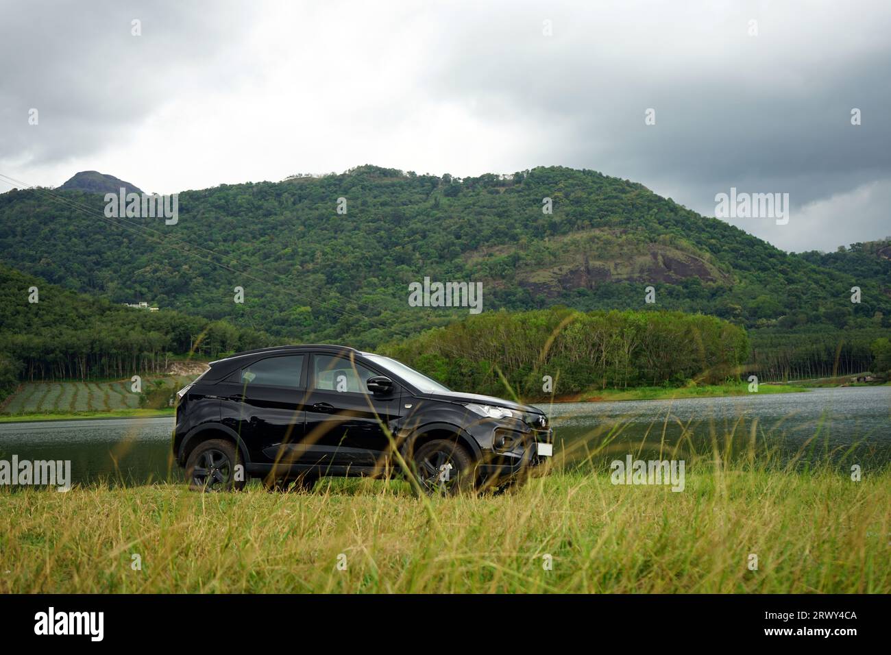 Black car parked near a lake with a hill background on a rainy season Stock Photo