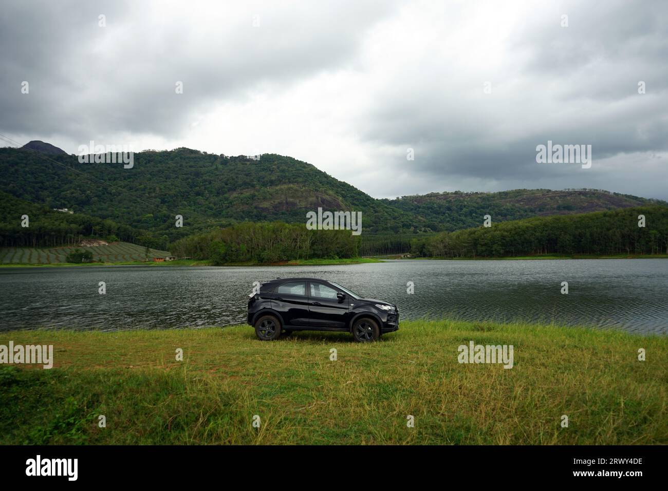 Black car parked near a lake with a hill background on a rainy season Stock Photo