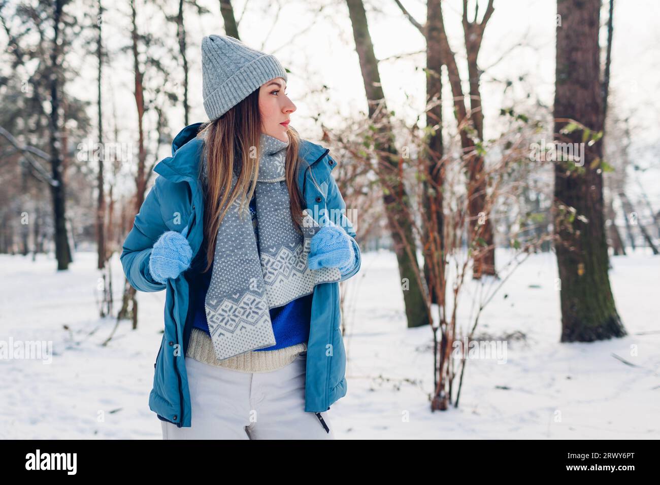 Portrait of young woman putting on blue coat walking in snowy