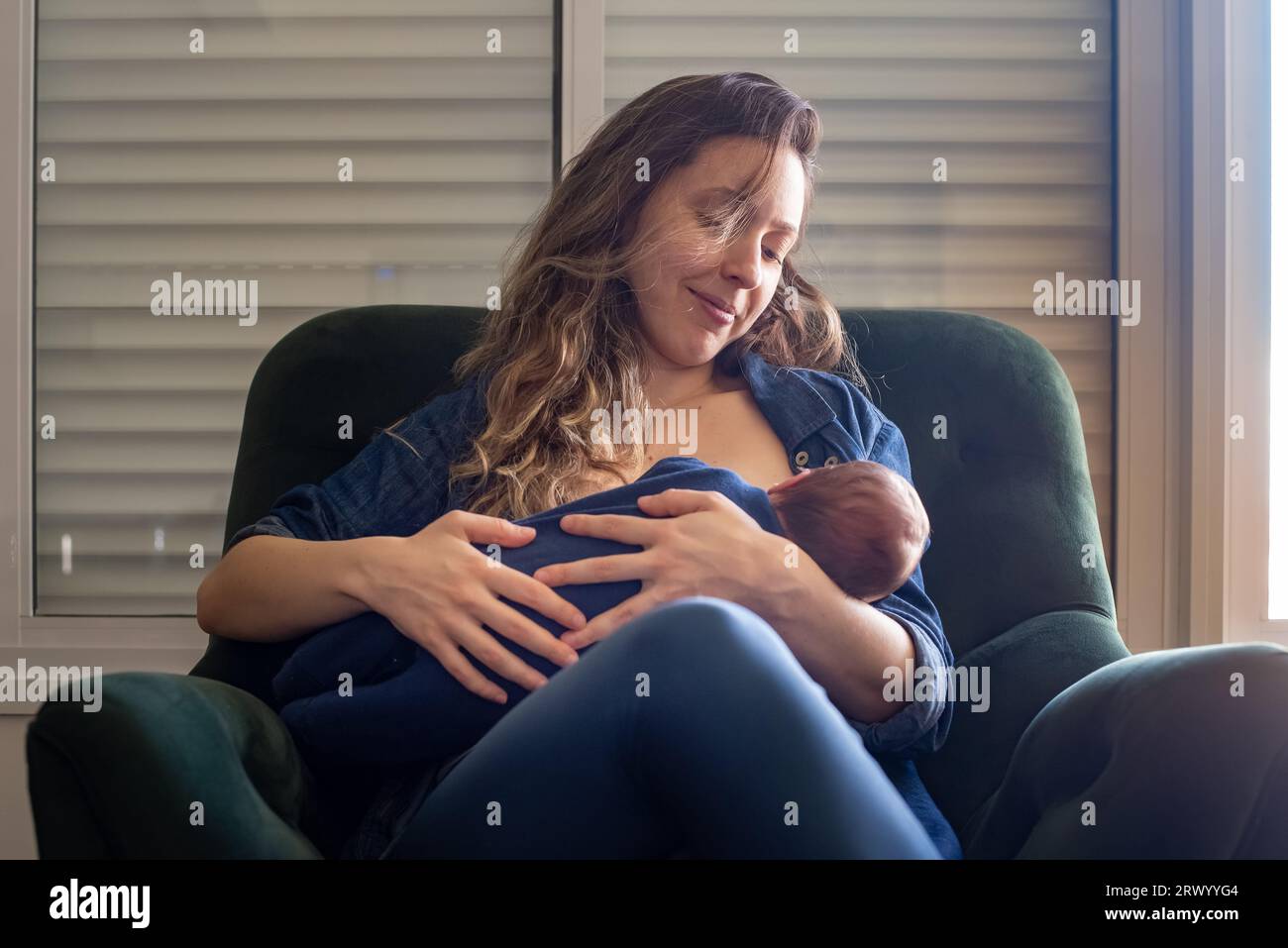 Happy mother breastfeeding her baby son while sitting on armchair at