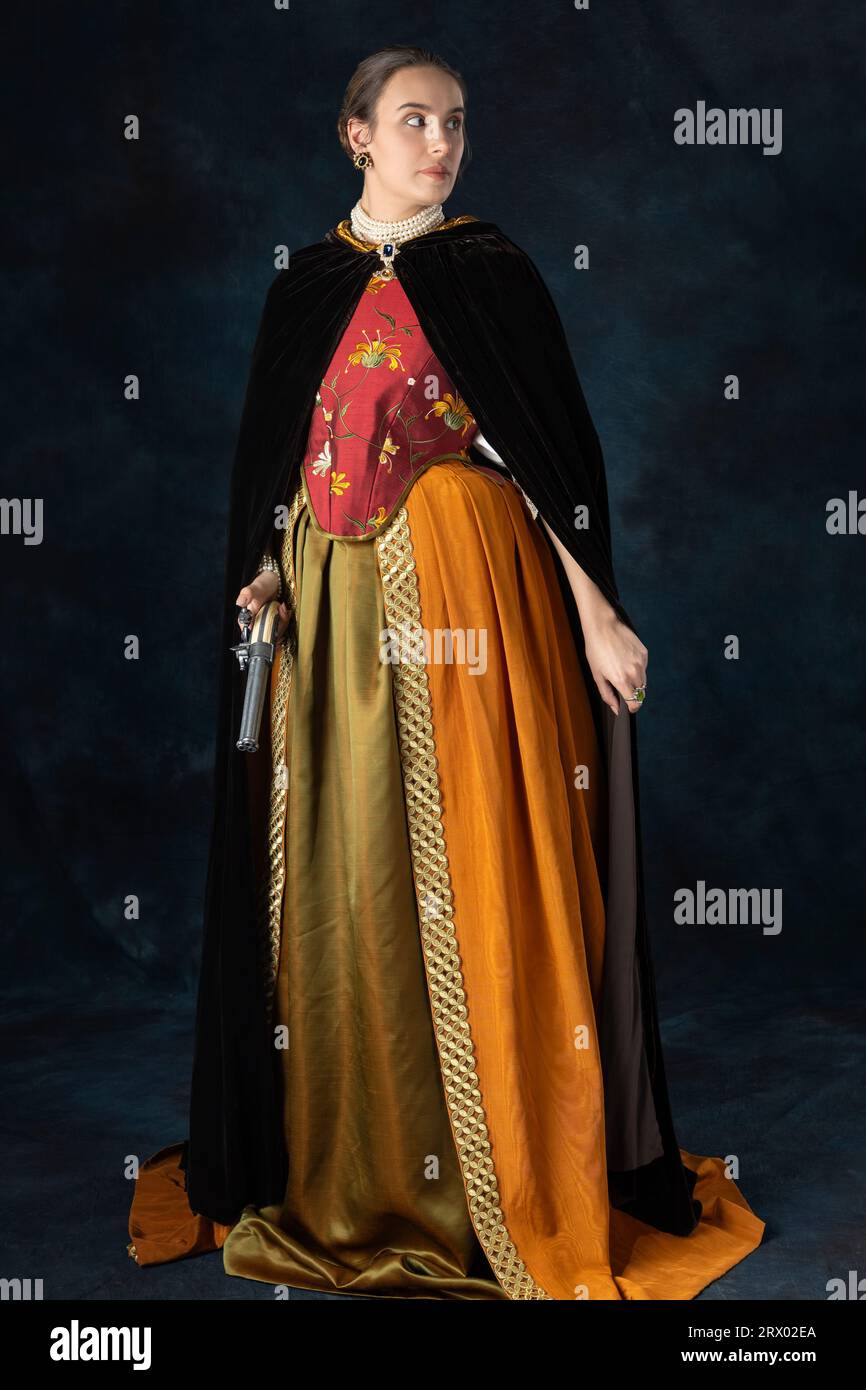 Woman in historical costume from Renaissance period with an embroidered bodice and silk velvet cloak against a studio backdrop Stock Photo