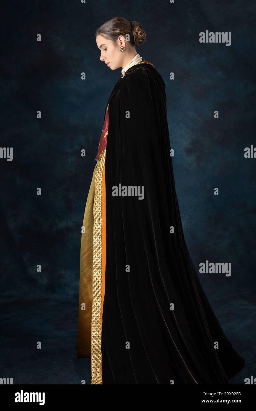 Woman in historical costume from Renaissance period with an embroidered bodice and silk velvet cloak against a studio backdrop Stock Photo