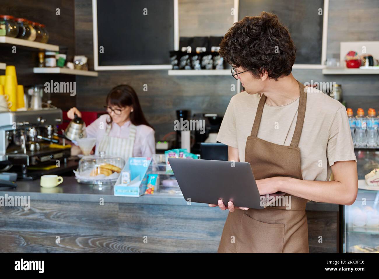 Young guy in an apron with laptop in his hands inside coffee shop cafeteria Stock Photo