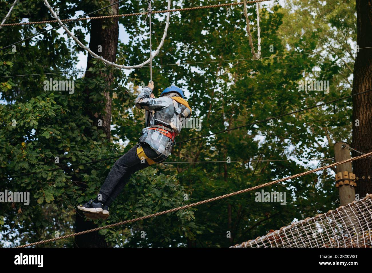 teenage boy going down on zipline in adventure park passing obstacle course. high rope park outdoors Stock Photo