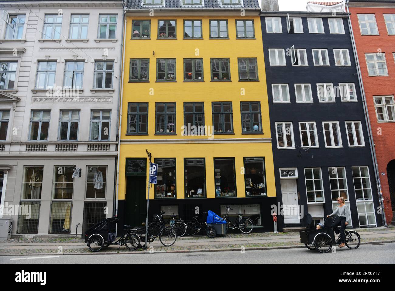 A Danish woman cycling in front of a Colorful building along Gammel Mønt in central Copenhagen, Denmark. Stock Photo