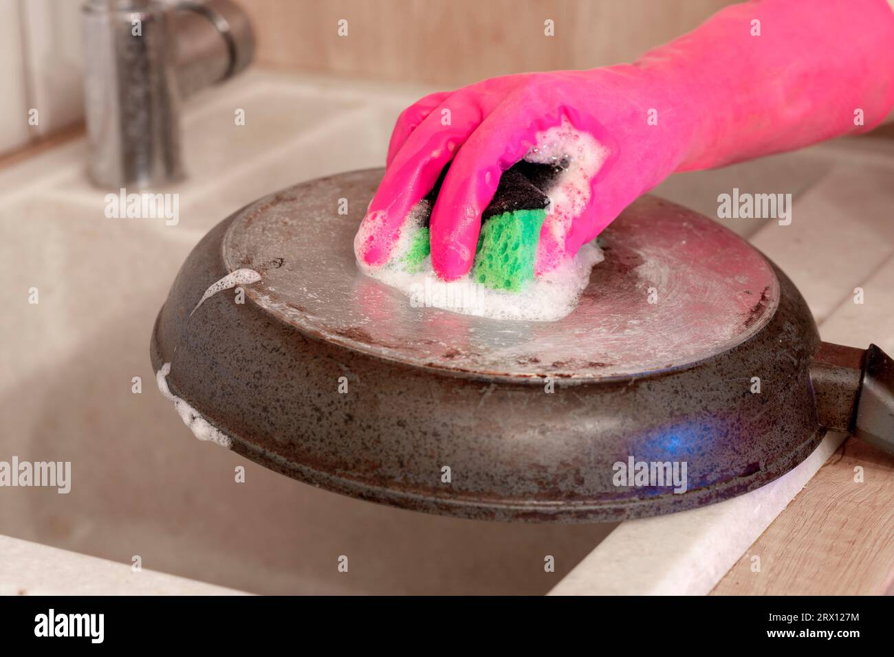 Cleaning a dirty frying pan with a kitchen sponge in the glove. Female