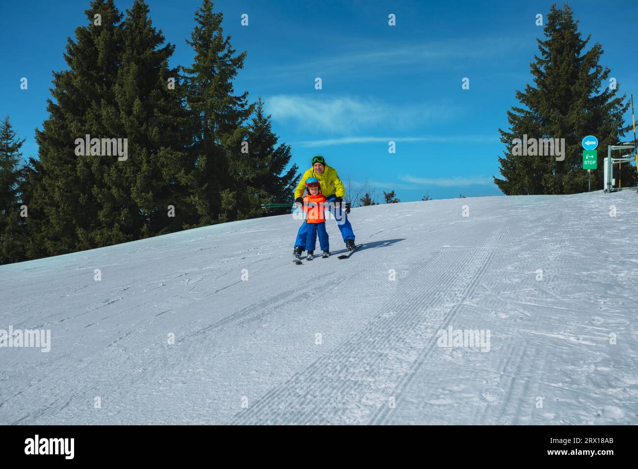 Dad teaches kid gliding behind holding ski poles together Stock Photo