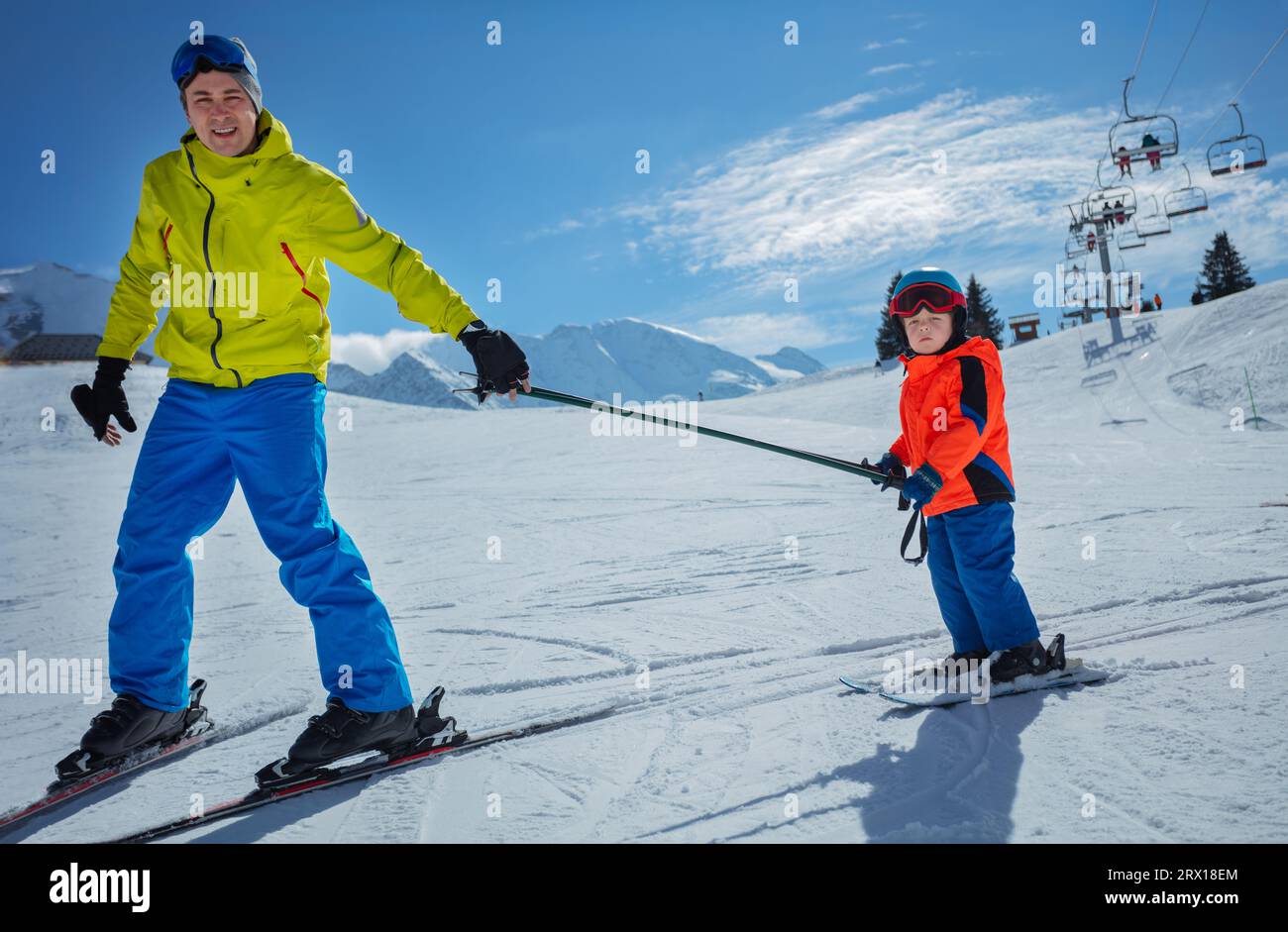 Dad go downhill teach child to ski connected by poles Stock Photo