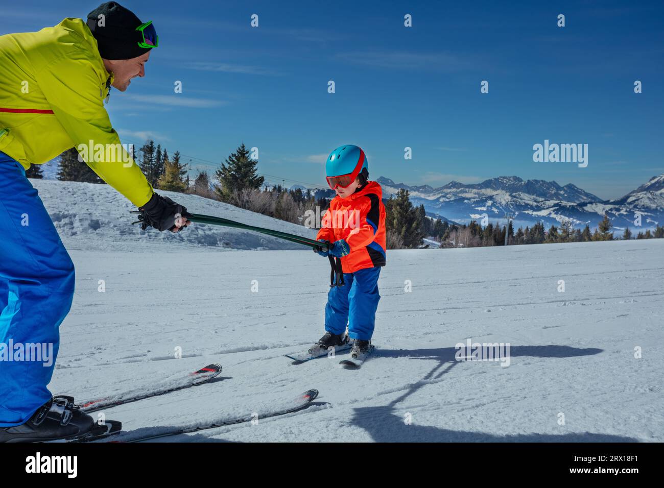 Man teach little boy child to ski moving holding poles together Stock Photo