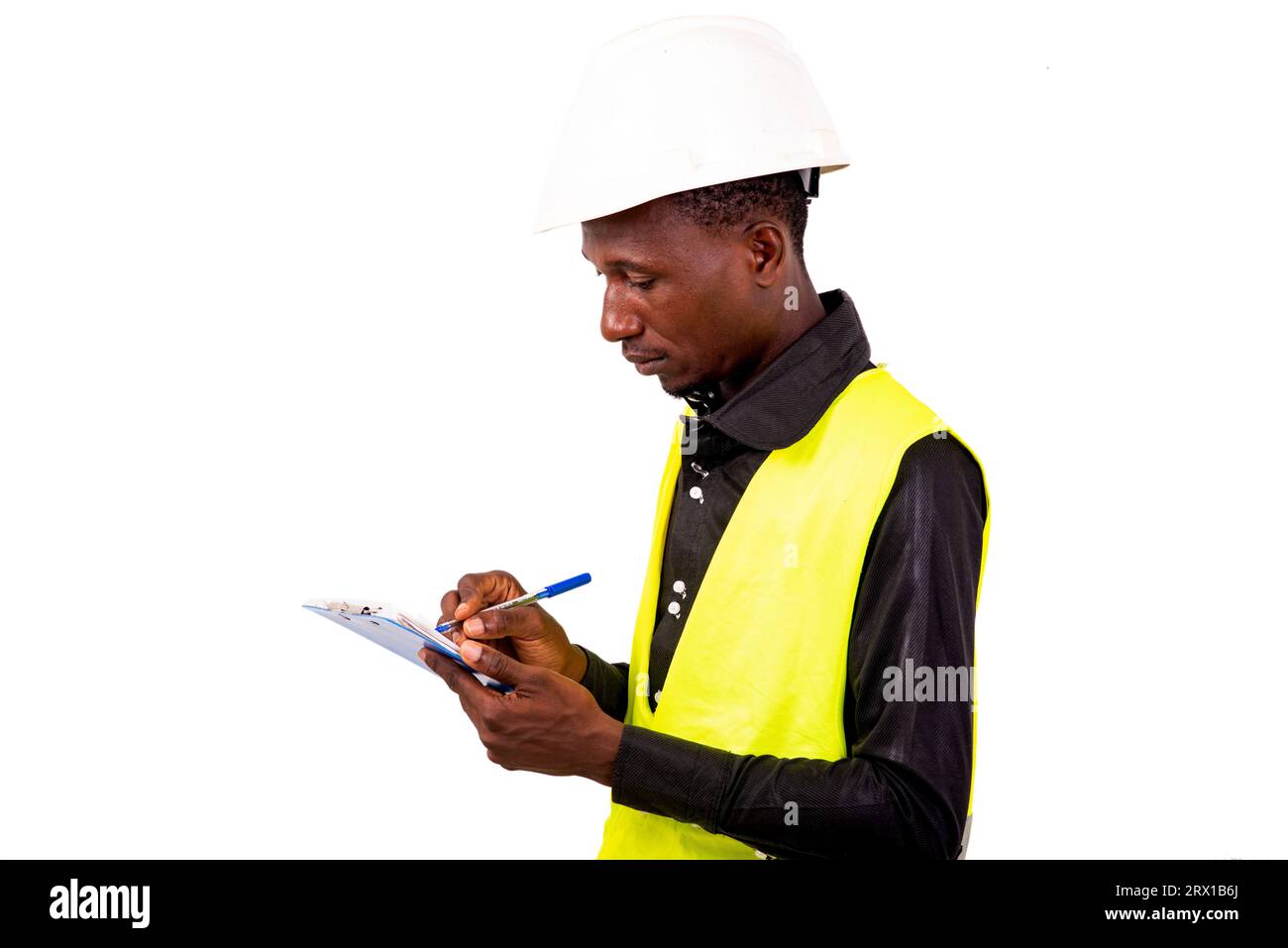young man inspector architect wearing green vest and safety helmet writing in clipboard while smiling. Stock Photo